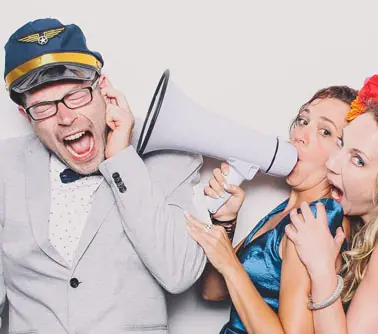 Trois invités en pleine improvisation devant le photobooth, casquette d'aviateur et porte-voix