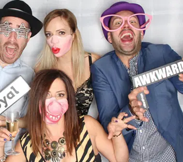 Quatre invités en soirée avec accessoires photobooth : lunettes colorées et pancartes humoristiques