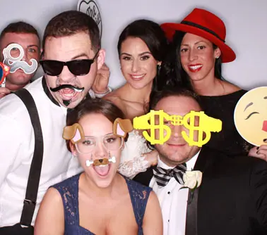 Groupe d'amis posant dans un photobooth avec lunettes géantes, moustaches et chapeau rouge