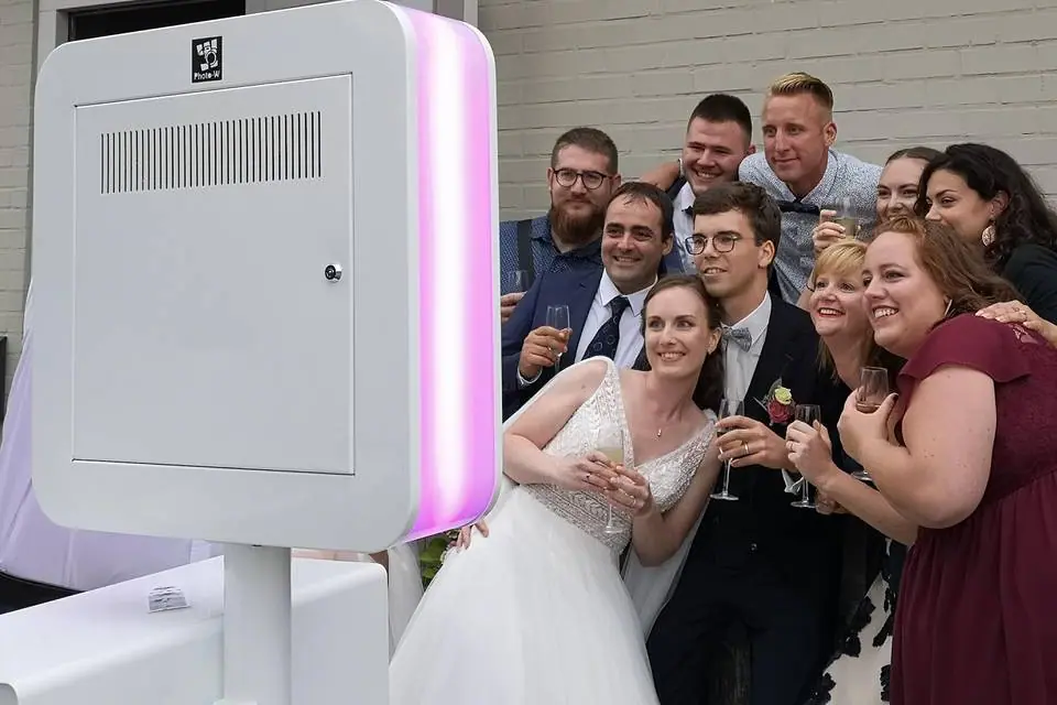Mariés et invités posés devant une borne photo à éclairage LED lors d'un mariage
